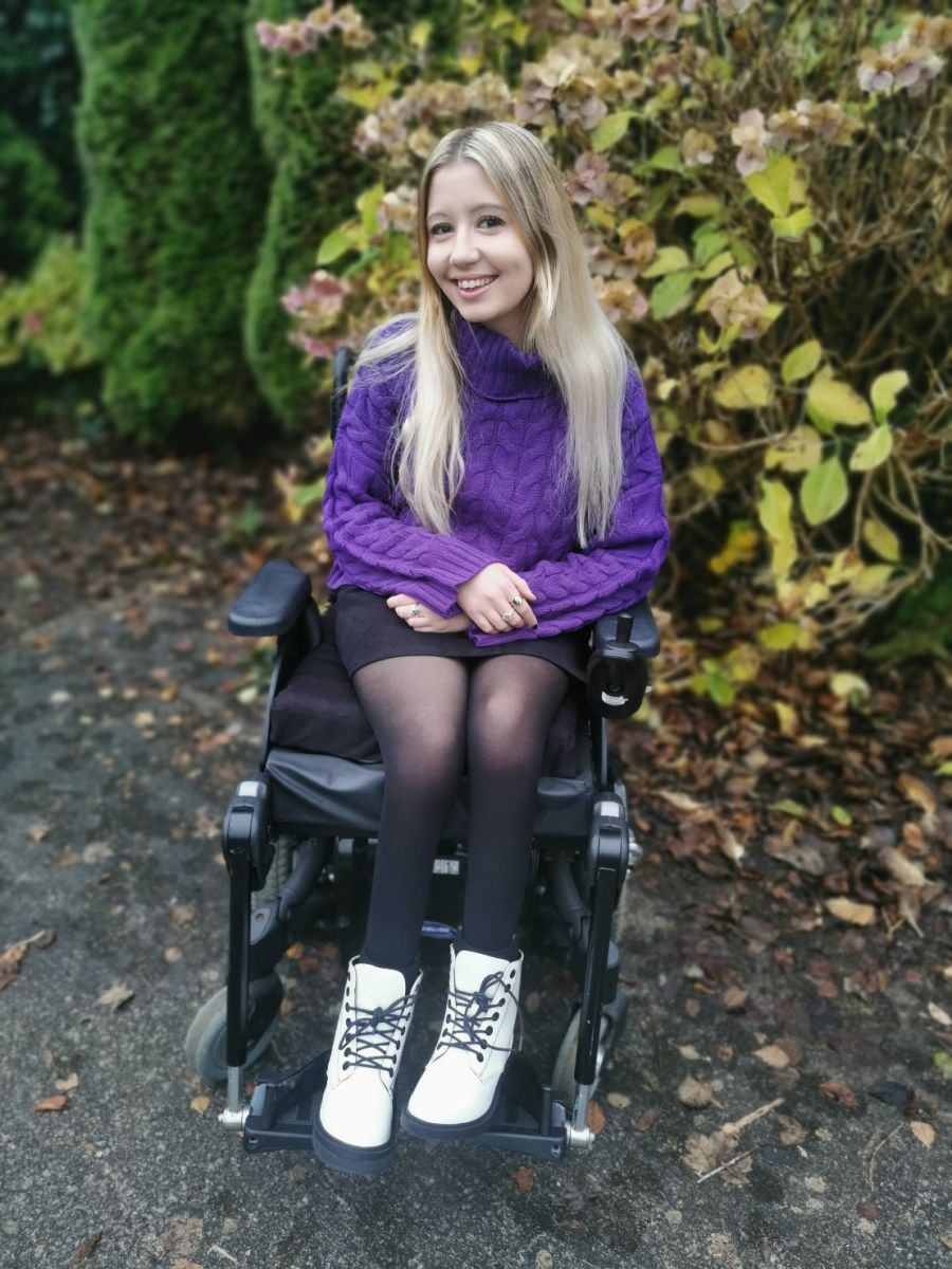 A Full body shot of Leesa. She is smiling for the camera, has long blonde hair and is in her wheelchair.