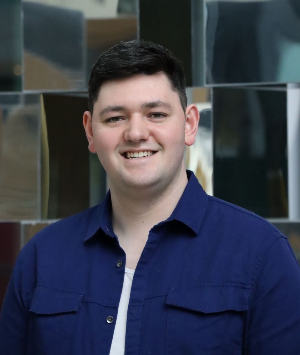 A headshot of Darragh. Darragh is smiling for the camera, he has short, dark hair and he is wearing a navy shirt